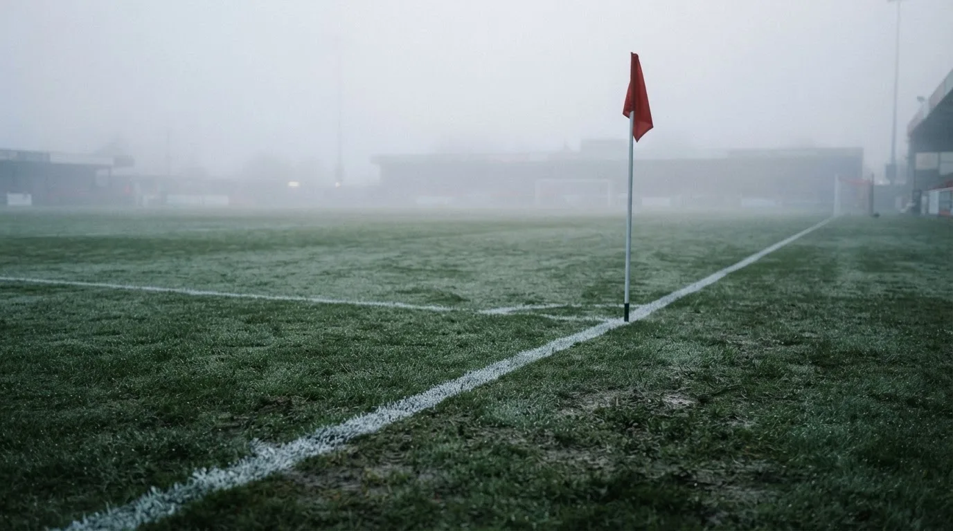 Der Rand eines Spielfelds mit weißer Linie und Eckfahne bei Nebel am frühen Morgen, ohne Menschen.
