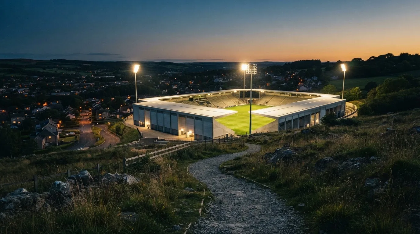 Ein Stadion unter Flutlicht, von einer Anhöhe aus gesehen, davor ein stiller Weg in der Dämmerung.