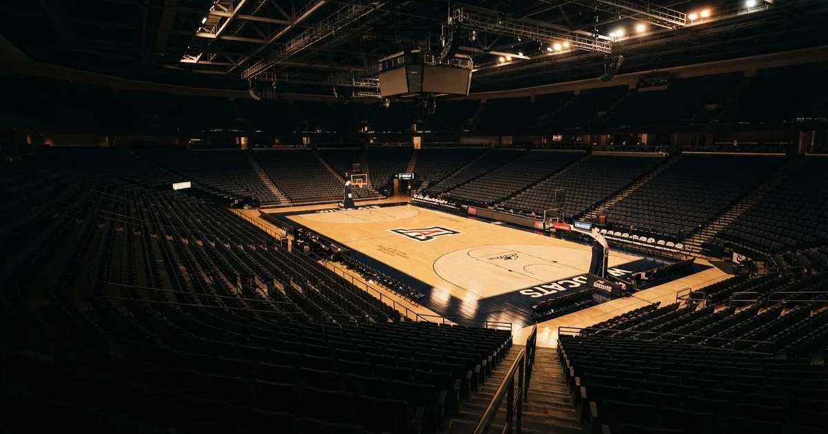 Eine leere Basketballhalle von einer oberen Tribünenreihe aus gesehen, Parkett und Körbe im Licht der Hallenstrahler.