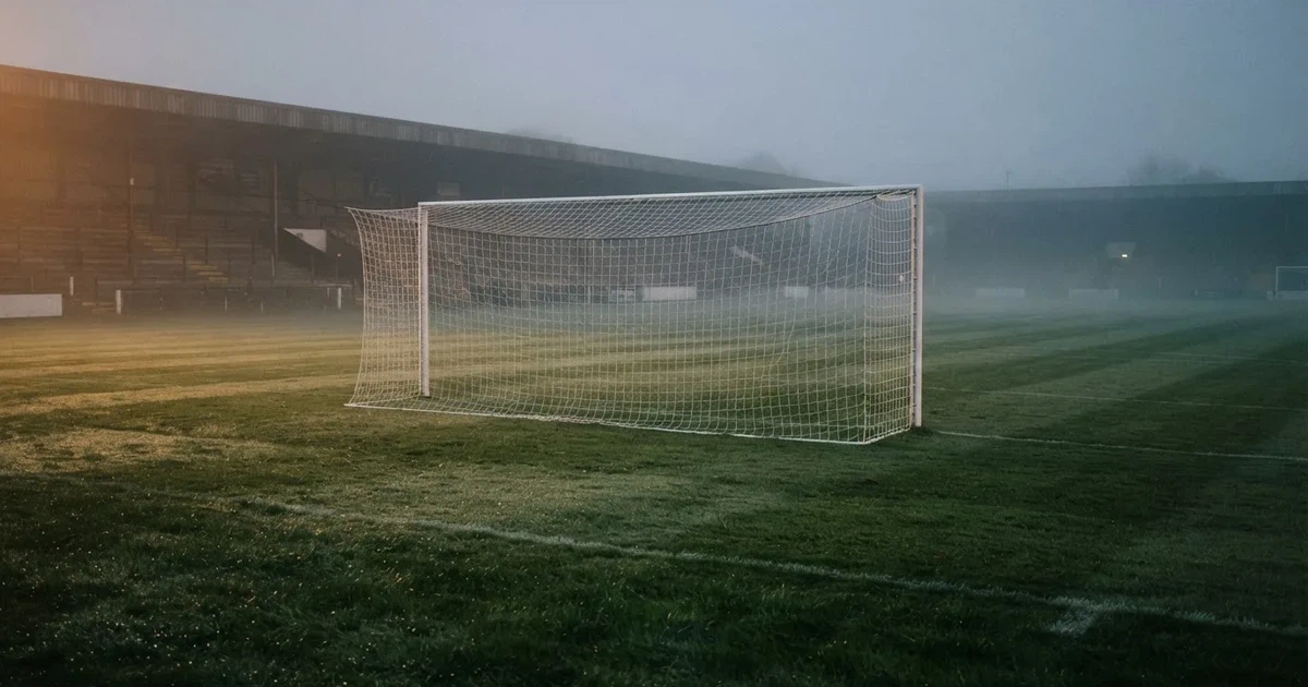 Ein Fußballtor mit Netz steht auf einem leeren Platz im Nebel der Morgendämmerung, der Rasen ist taufeucht.