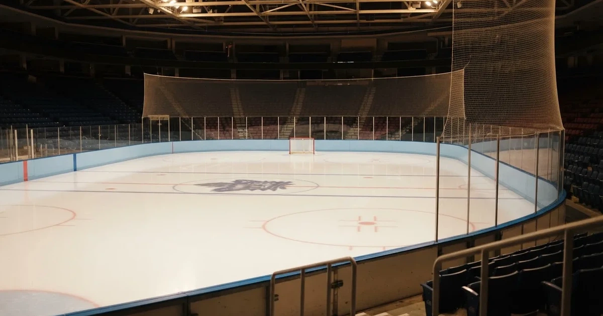 Eine Eishockeyhalle von der Tribüne aus gesehen, spiegelglatte Eisfläche, Banden ohne Schriftzüge, helles Flutlicht.