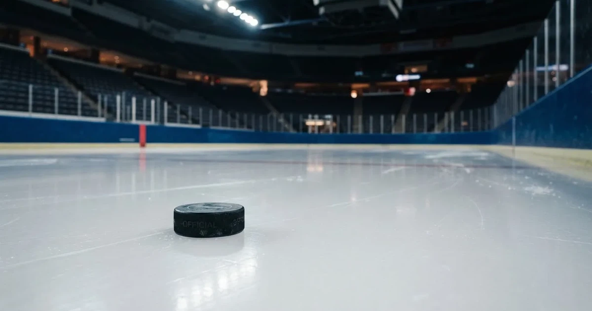 Eine leere Eisfläche in einer Halle mit Banden und Flutlicht, auf dem Eis liegt ein einzelner Puck.