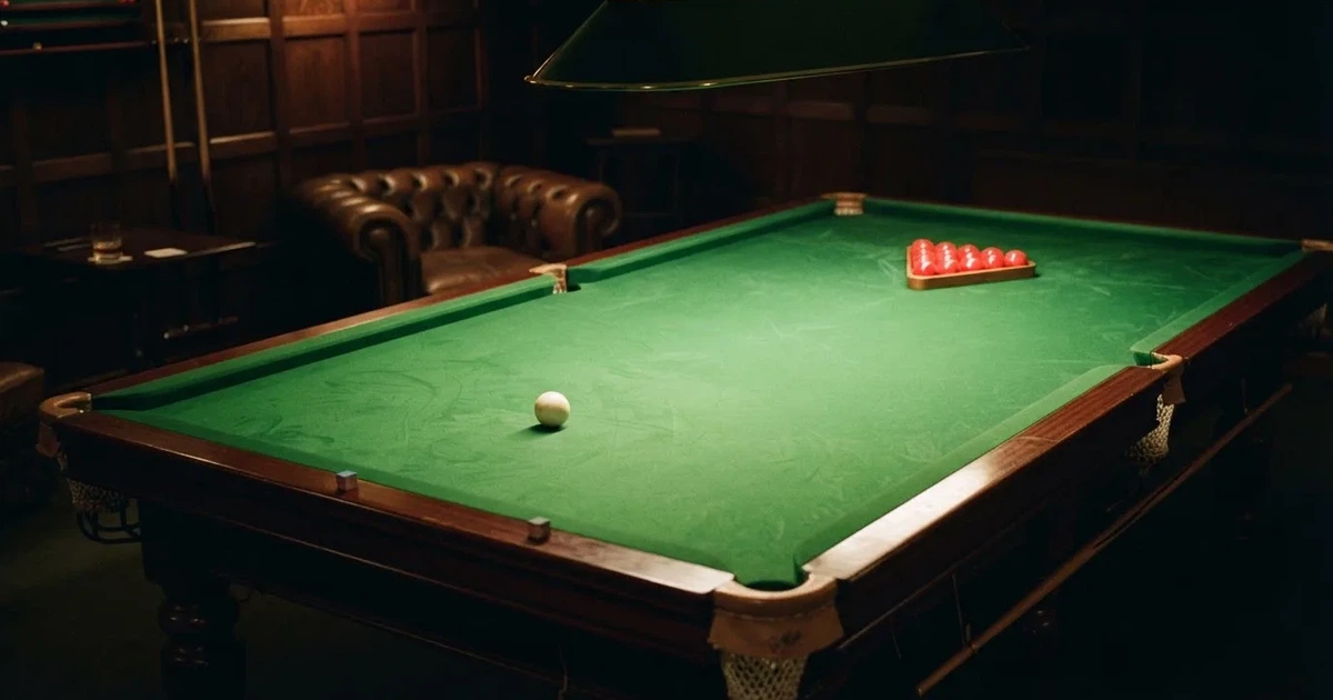 Ein Snookertisch mit grünem Tuch und aufgebauten roten Kugeln in einem abgedunkelten Raum unter einer hängenden Lampe.