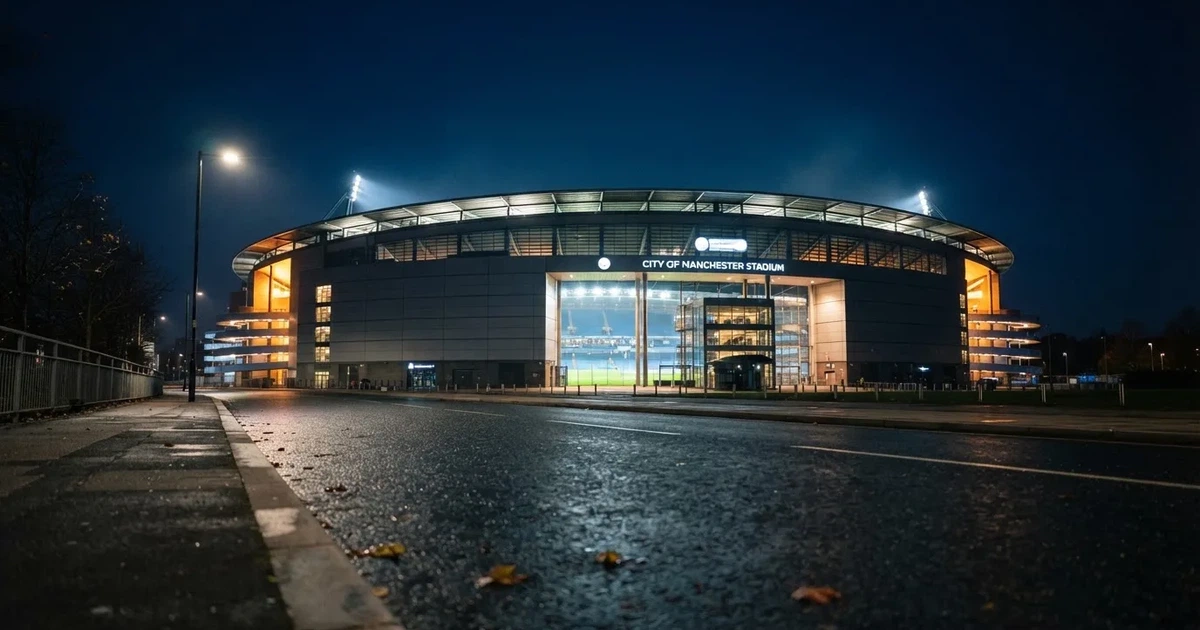 Ein hell erleuchtetes Fußballstadion bei Nacht aus der Ferne gesehen, über dem Dach ein klarer Himmel, davor eine leere Straße.